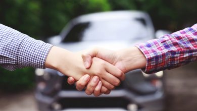 A close-up of two people shaking hands with a car in the background.